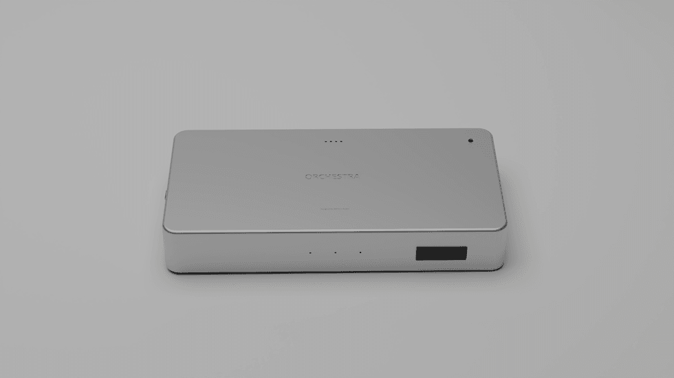 Close-up of a sleek silver rectangular device labeled "ORCHESTRA" — the portable intelligent hub that runs the operating system for Spatial Intent Fusion