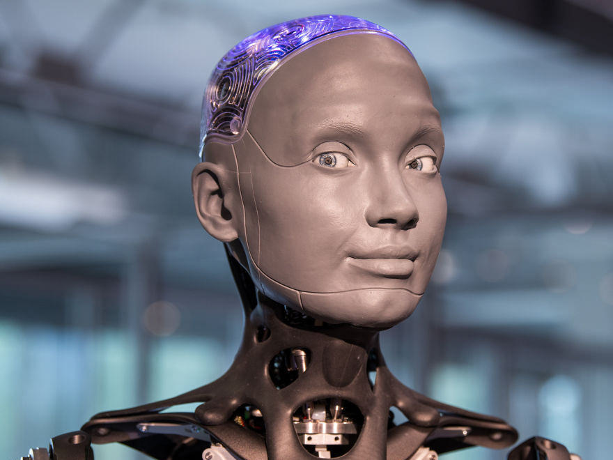 Side-by-side: Engineered Arts Ameca humanoid head and shoulders, right: Unitree G1 standing. Both robots at human scale.